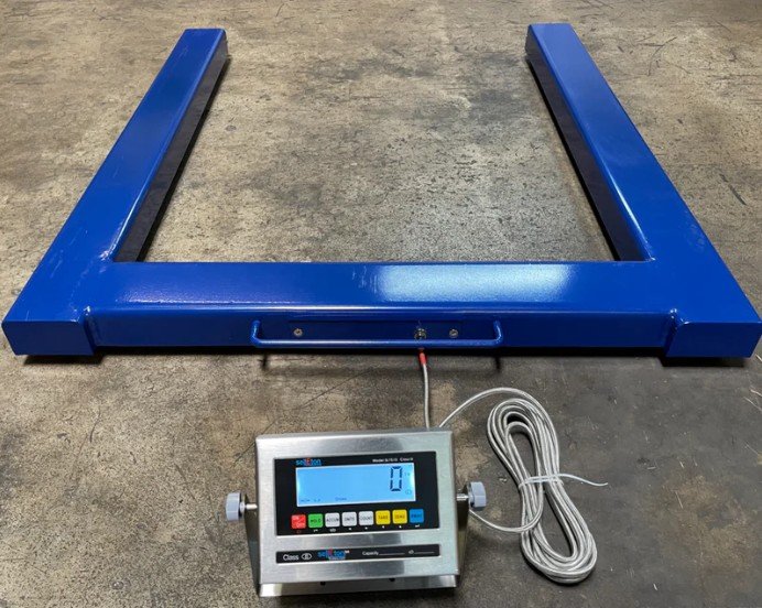 U-frame pallet scale with open arms sliding under a loaded pallet on a warehouse floor for in-place weighing