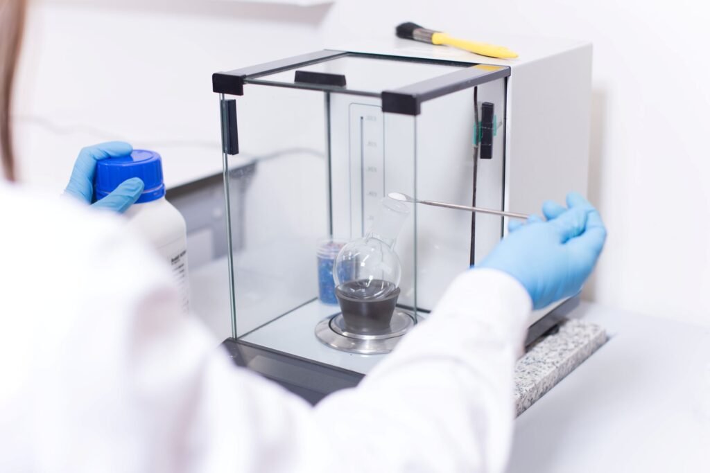 Scientist using an analytical laboratory balance with draft shield to weigh a small chemical sample in a research lab