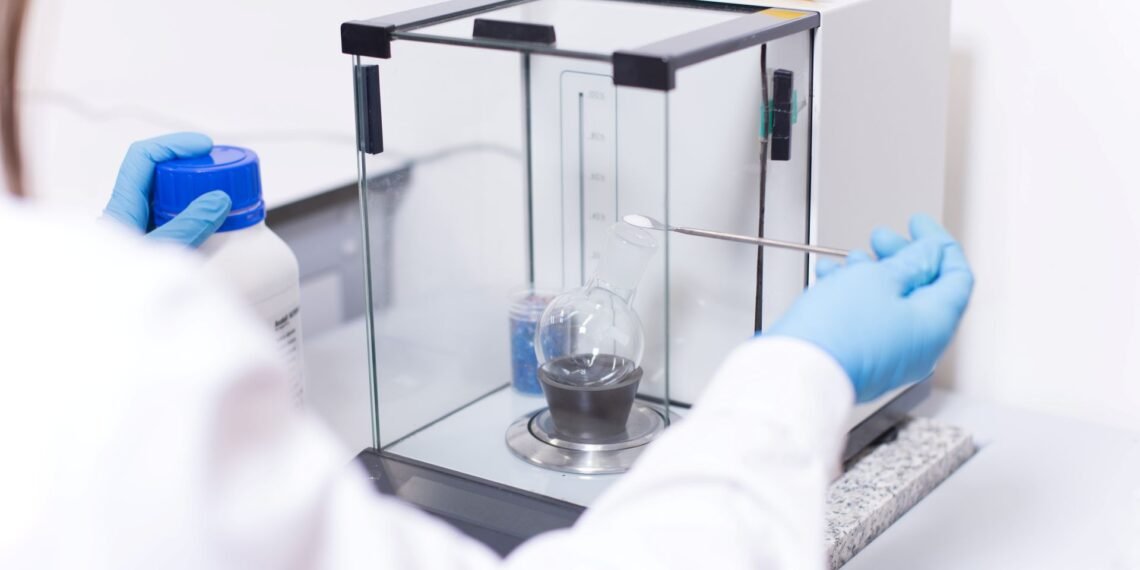 Scientist using an analytical laboratory balance with draft shield to weigh a small chemical sample in a research lab