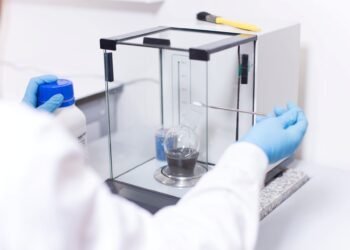 Scientist using an analytical laboratory balance with draft shield to weigh a small chemical sample in a research lab