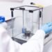 Scientist using an analytical laboratory balance with draft shield to weigh a small chemical sample in a research lab