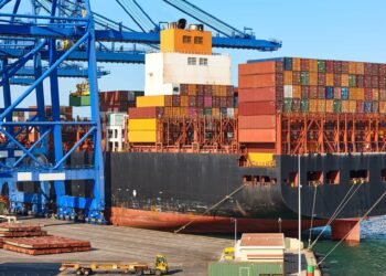 Loaded shipping containers being lifted by crane at a port terminal before vessel loading under SOLAS VGM requirements