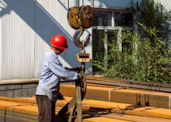 Heavy industrial crane scale suspended from a crane hook weighing a large steel component in a manufacturing facility