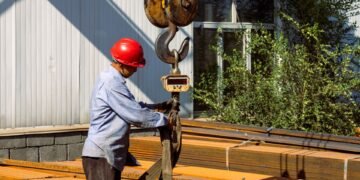 Heavy industrial crane scale suspended from a crane hook weighing a large steel component in a manufacturing facility