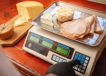 NTEP-certified deli counter scale with dual display showing weight and price while operator slices turkey for customer