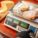 NTEP-certified deli counter scale with dual display showing weight and price while operator slices turkey for customer