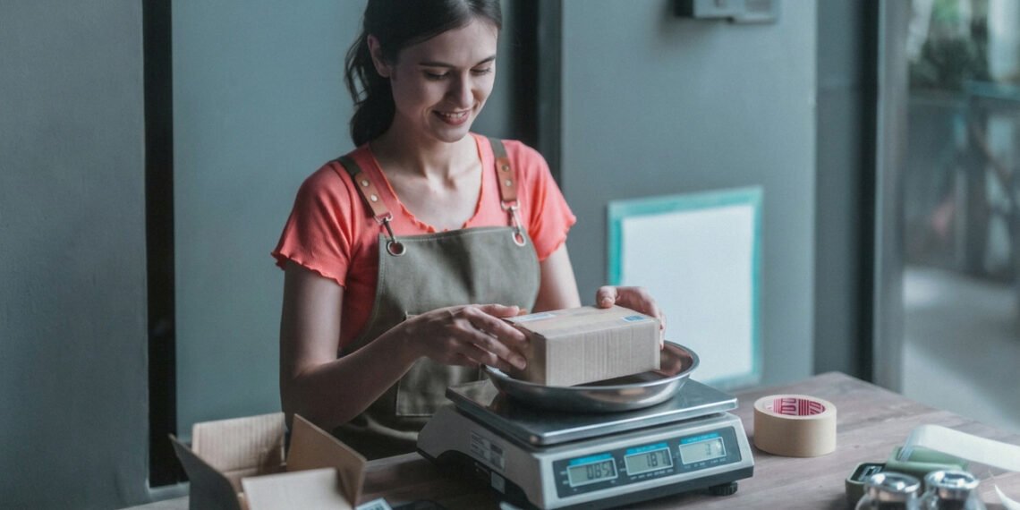 Small business owner weighing a package on a bench top parcel scale at an ecommerce packing station