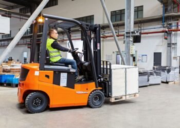 Forklift with carriage-mounted scale weighing a pallet load in a warehouse distribution center with weight displayed on cab indicator