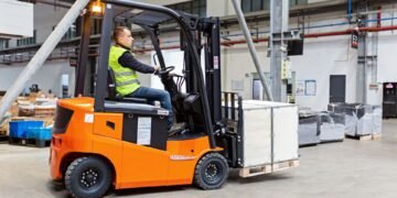 Forklift with carriage-mounted scale weighing a pallet load in a warehouse distribution center with weight displayed on cab indicator