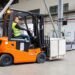 Forklift with carriage-mounted scale weighing a pallet load in a warehouse distribution center with weight displayed on cab indicator