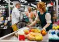 Cashier at a grocery store checkout lane using a POS-integrated scale to weigh fresh produce and automatically calculate the price for a customer transaction