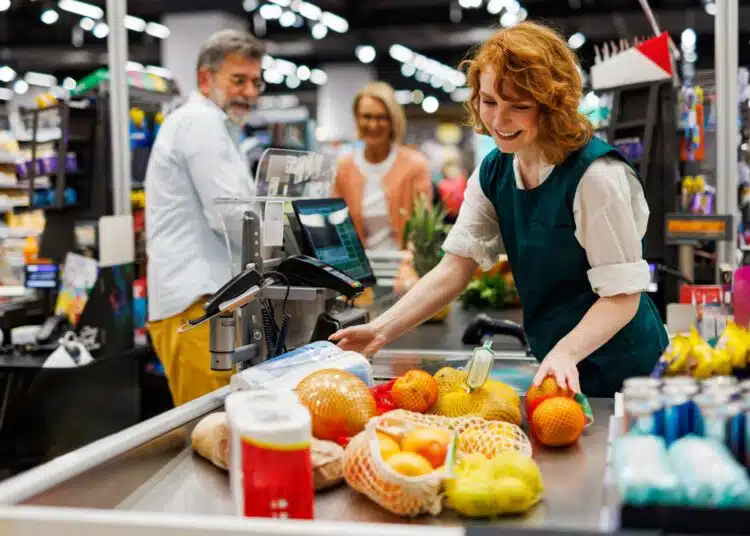 Cashier at a grocery store checkout lane using a POS-integrated scale to weigh fresh produce and automatically calculate the price for a customer transaction