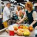 Cashier at a grocery store checkout lane using a POS-integrated scale to weigh fresh produce and automatically calculate the price for a customer transaction