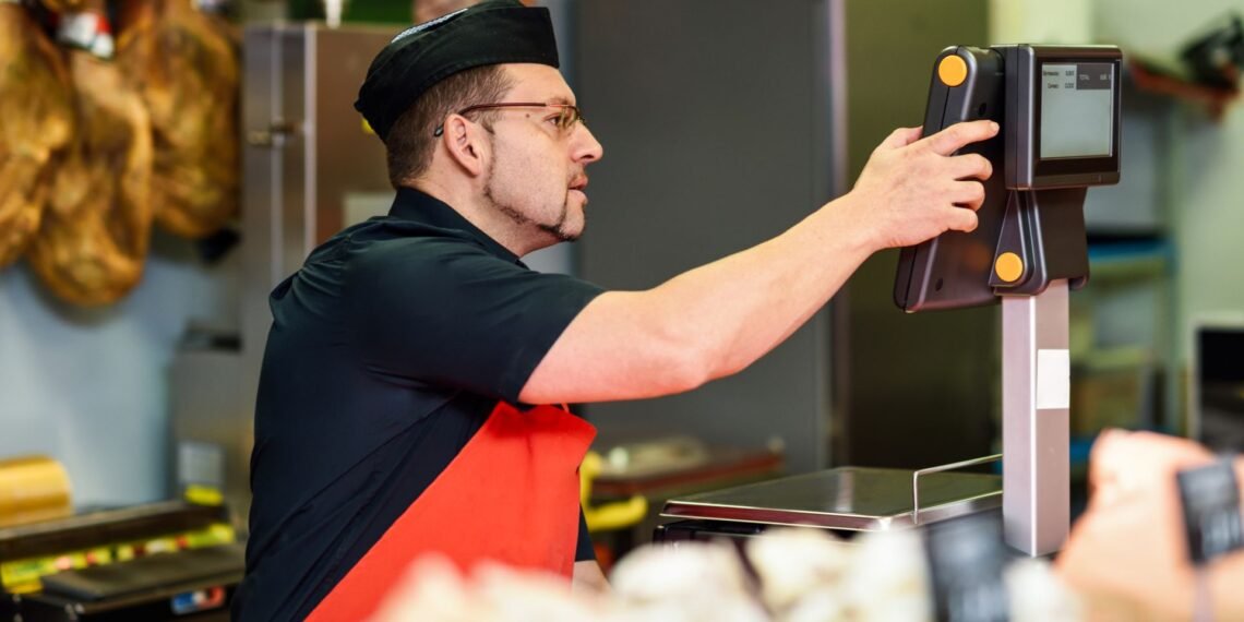 Label printing scale at a deli counter printing a thermal barcode label with product name weight price and sell-by date on pre-packaged deli meat