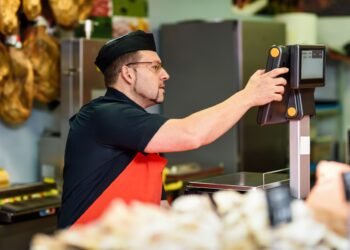 Label printing scale at a deli counter printing a thermal barcode label with product name weight price and sell-by date on pre-packaged deli meat