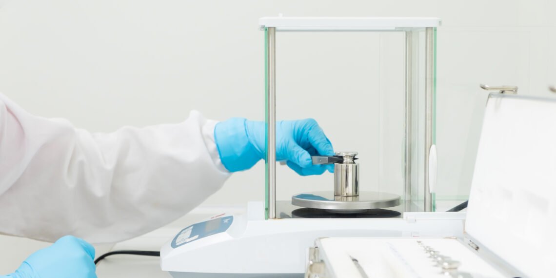Laboratory technician performing external calibration of an analytical balance using OIML certified reference weights in a pharmaceutical QC laboratory