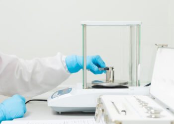 Laboratory technician performing external calibration of an analytical balance using OIML certified reference weights in a pharmaceutical QC laboratory