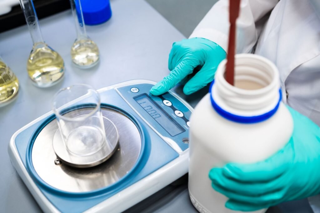 Laboratory analyst using the tare function on an analytical balance to zero out the weight of a glass beaker before weighing a chemical reagent