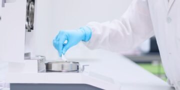 Laboratory technician placing a sample in a halogen moisture analyzer in a pharmaceutical quality control laboratory