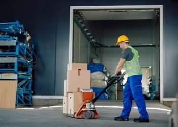 Warehouse operator using a digital pallet jack scale to weigh a loaded pallet during transport in a distribution center