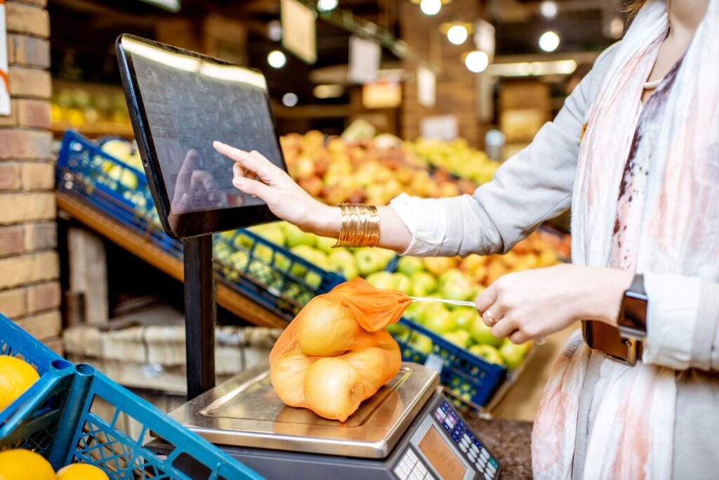 Customer using a grocery store self-checkout kiosk with integrated scale to weigh and price fresh produce by selecting the item from a visual PLU menu