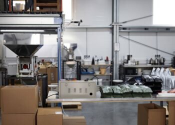 Warehouse operator weighing a fully sealed shipping package on a digital scale connected to shipping software at a packing station