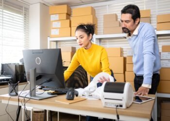 Warehouse worker at a packing station using a calibrated shipping scale to weigh a sealed package before generating a shipping label