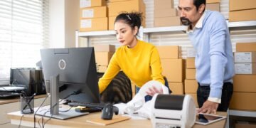 Warehouse worker at a packing station using a calibrated shipping scale to weigh a sealed package before generating a shipping label