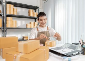 Business owner selecting a digital shipping scale at a warehouse packing station with packages ready for dispatch
