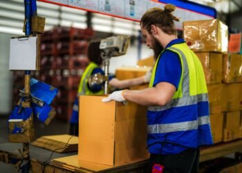 Digital shipping scale on a warehouse packing station bench with packages being weighed before dispatch