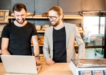 Worker at a warehouse shipping station weighing a cardboard box on a digital shipping scale before labeling