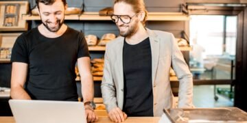 Worker at a warehouse shipping station weighing a cardboard box on a digital shipping scale before labeling