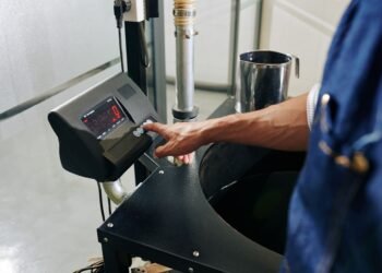 Operator pressing the tare button on a digital shipping scale at a warehouse packing station with an empty shipping box on the platform