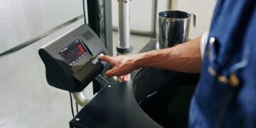 Operator pressing the tare button on a digital shipping scale at a warehouse packing station with an empty shipping box on the platform