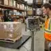 Warehouse operator reading the digital display on an industrial floor scale showing gross weight net weight and stability indicator