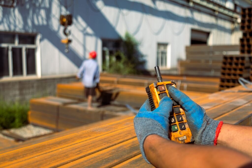 Industrial worker holding a wireless handheld receiver displaying the crane scale weight reading while a load is lifted overhead