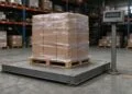 Floor scale with a shrink-wrapped pallet on the steel platform and a post-mounted weight indicator in a warehouse