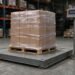 Floor scale with a shrink-wrapped pallet on the steel platform and a post-mounted weight indicator in a warehouse