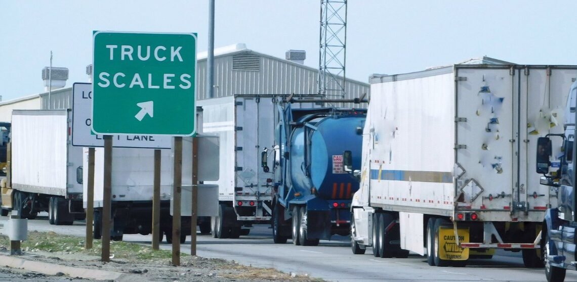 Semi-trucks lined up at a highway weigh station where truck axle weight limits are checked