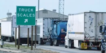Semi-trucks lined up at a highway weigh station where truck axle weight limits are checked